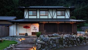 A traditional Japanese building with a wooden exterior, a stone pathway leading to the entrance, and a red umbrella.