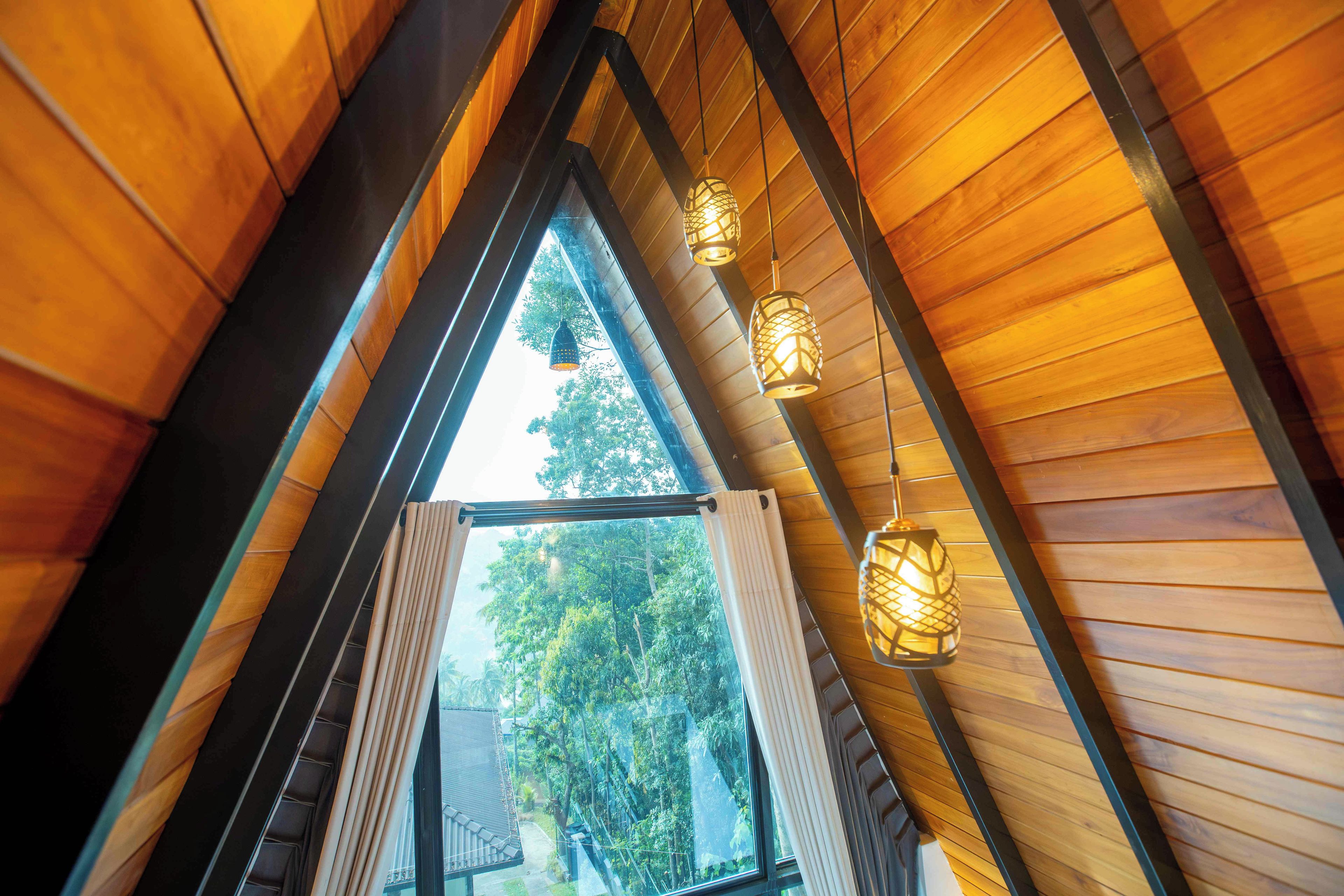 Un interior de madera con techo inclinado, una ventana con cortinas y lámparas colgantes.