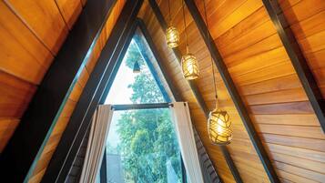 Un interior de madera con techo inclinado, una ventana con cortinas y lámparas colgantes.