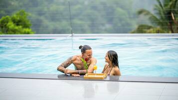 A couple in a swimming pool with a wooden tray and a drink.
