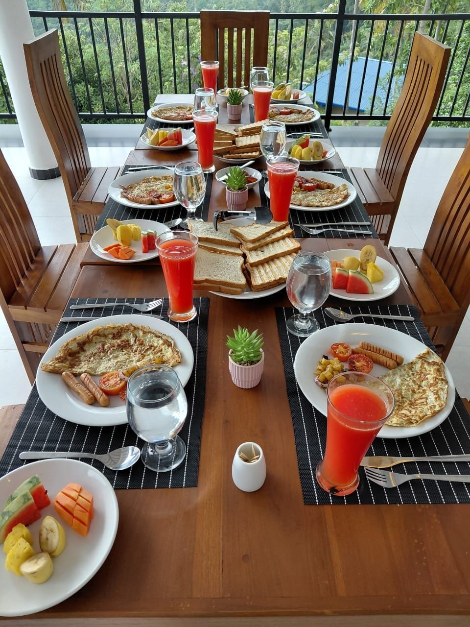 Tavolo imbandito con prodotti per la colazione, tra cui pane tostato, uova e frutta, su un balcone con vista.