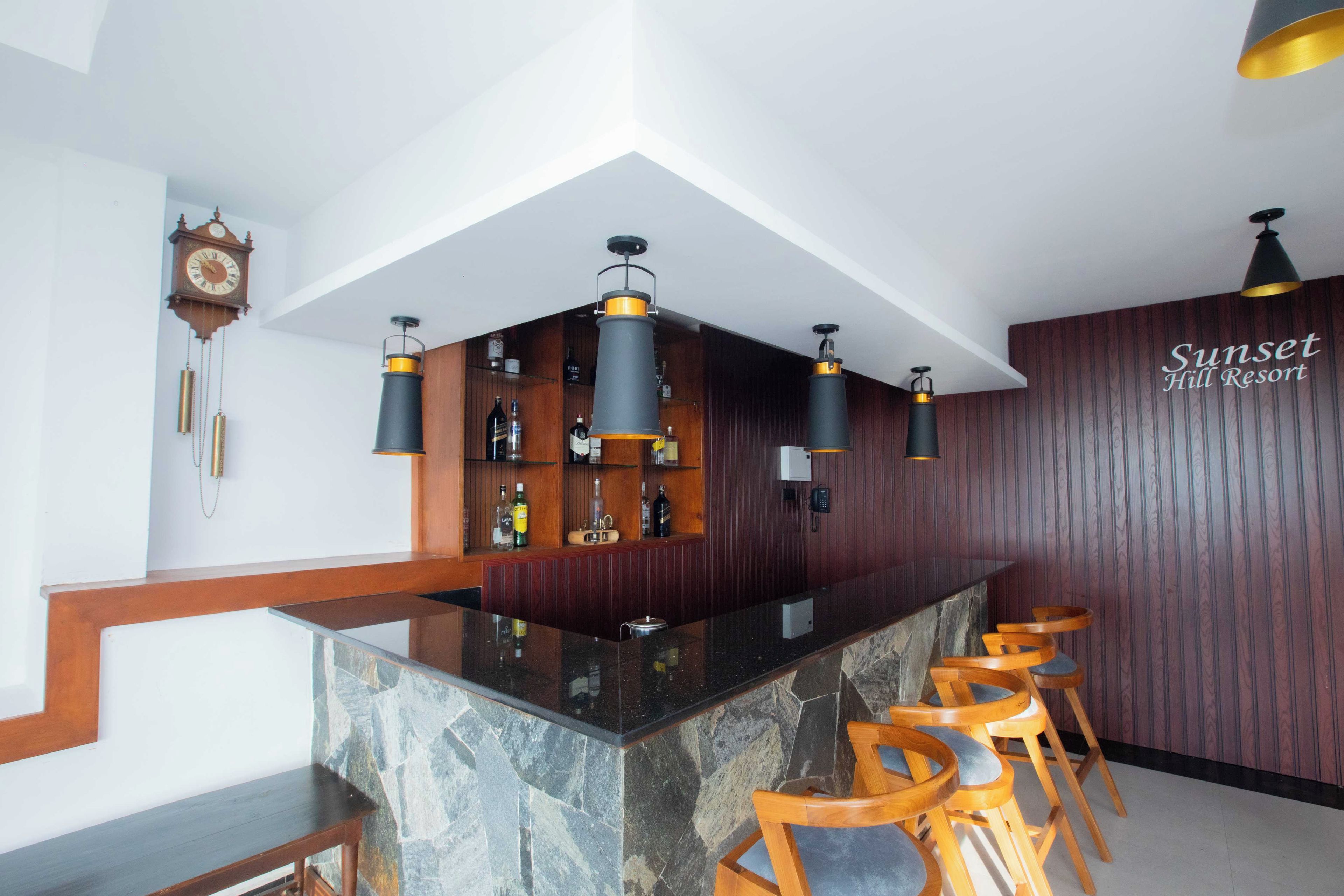 Una zona de bar con mostrador de piedra, taburetes de madera y un reloj en la pared.