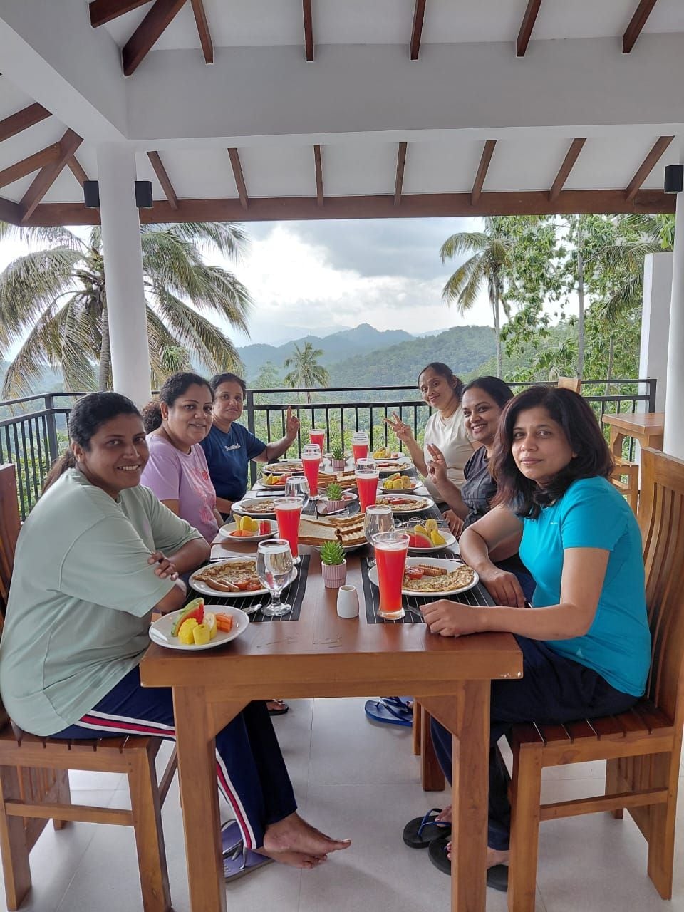 Un grupo de personas cenando en una mesa al aire libre con vistas a palmeras y montañas.