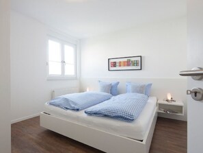 A bedroom with a bed, a nightstand, a framed picture on the wall, and a window. - Seilerstr./knyphausenstr.26a - Nele (Norderney)