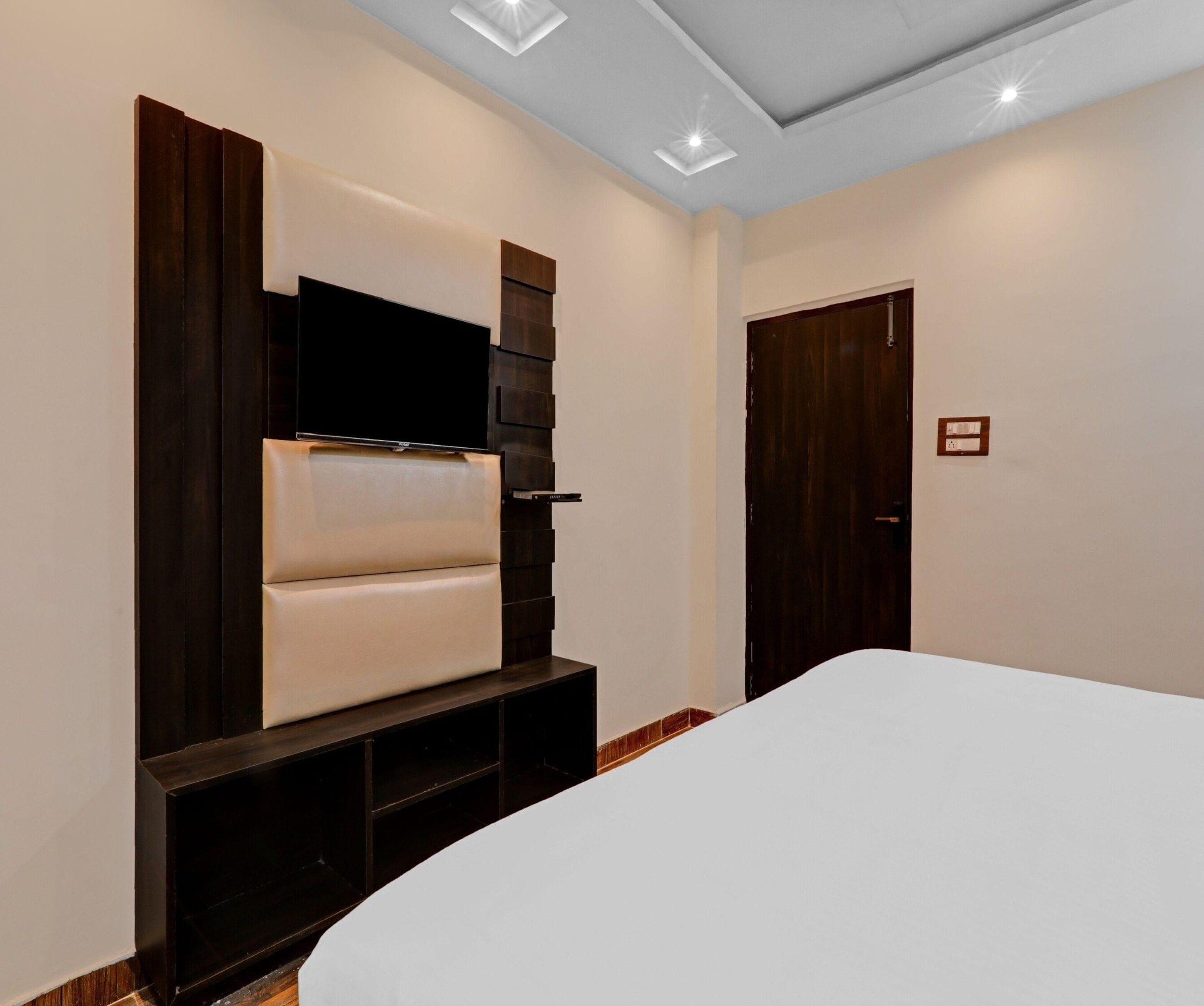 Een slaapkamer met een bed, een aan de muur bevestigde televisie en een deur.