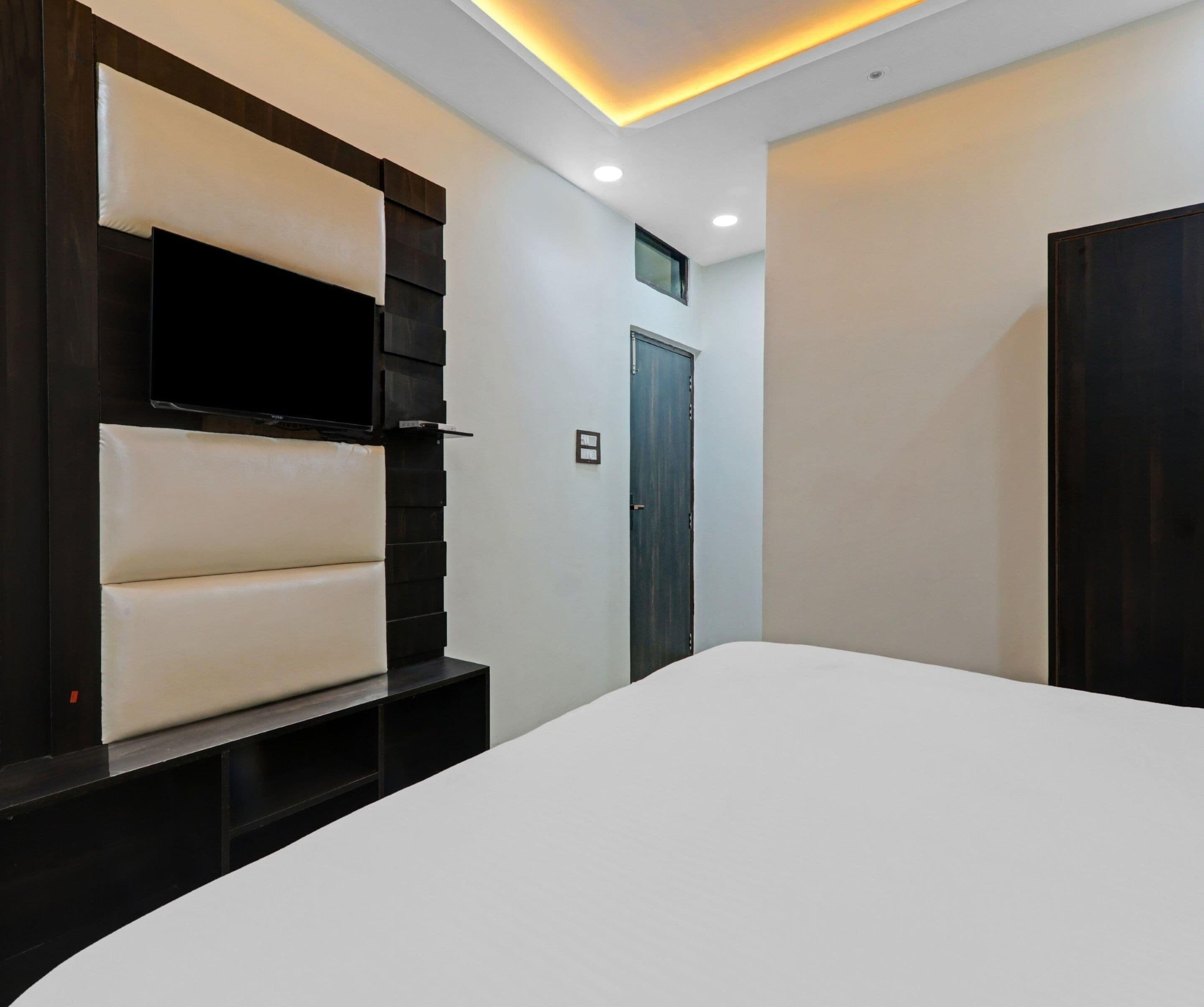 A modern hotel room with a large bed, a mounted TV, and a dark wooden wardrobe.