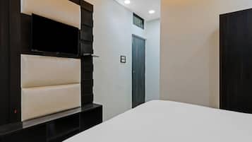 A modern hotel room with a large bed, a mounted TV, and a dark wooden wardrobe.