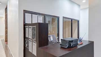 Una recepción con carteles informativos, una mampara de vidrio y un escritorio con una bolsa negra y bolígrafos.