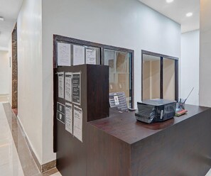 A reception desk with a dark wood finish, a glass partition, and various informational posters. - Classic Hotel Crystal Grand (Kanpur)