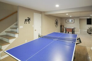 A room with a ping pong table, a staircase, a door, and a wall clock. - 13-Acre Vermont Estate w/ Hot Tub & Game Room (West Dover)