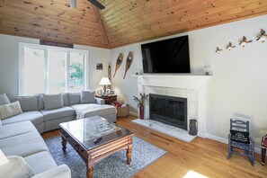 Un salon comprenant un canapé, une table basse, une cheminée et un téléviseur fixé au mur.
