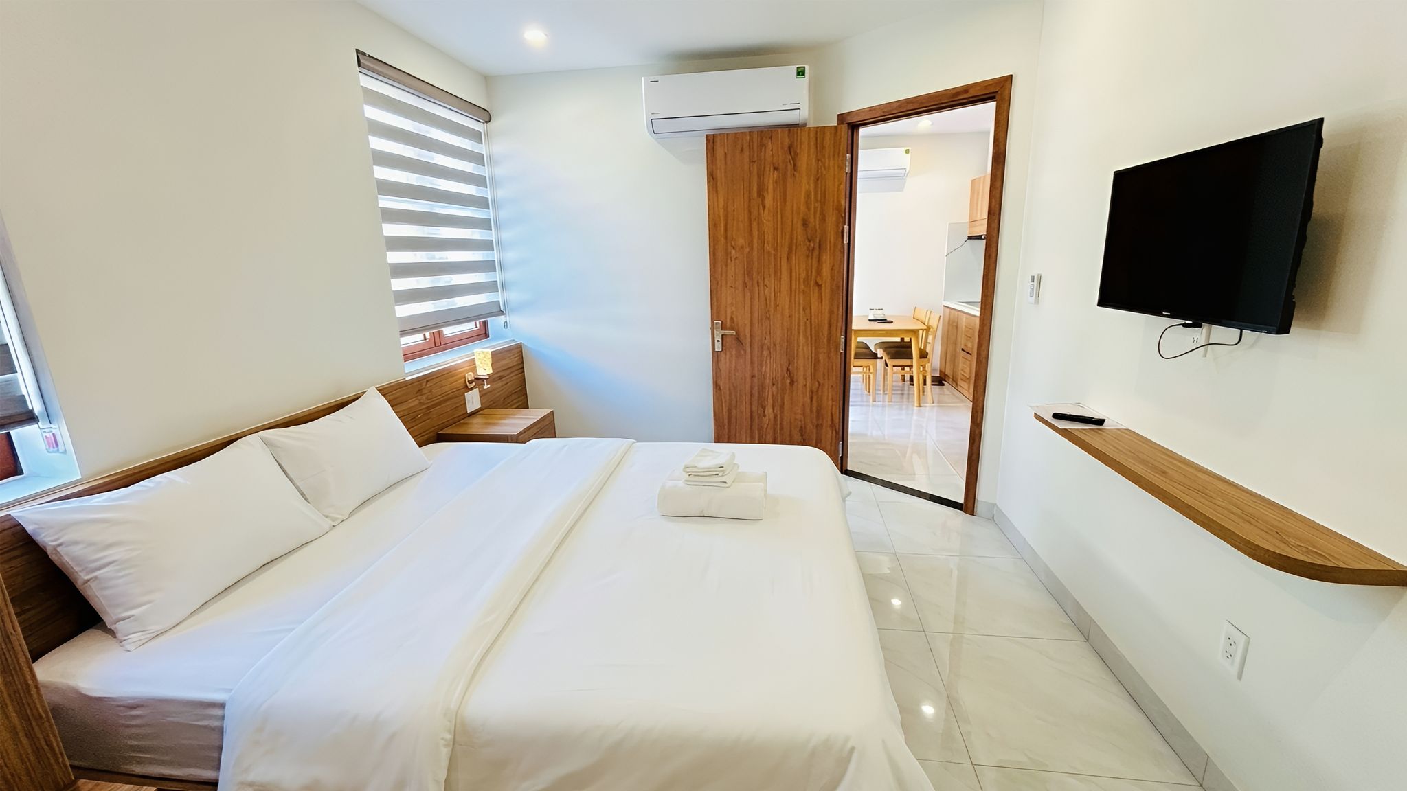 A hotel room with a bed, bedside table, wall-mounted TV, and an air conditioning unit.