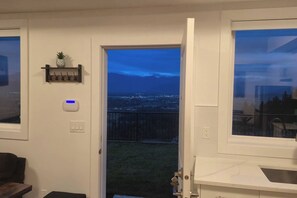 A room with a door leading to a balcony with a city view at night.