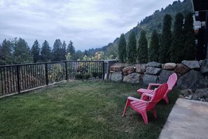 A patio with a metal fence, two red chairs, and a stone wall. - Elevated Horizon Retreat - Royal (Chilliwack)