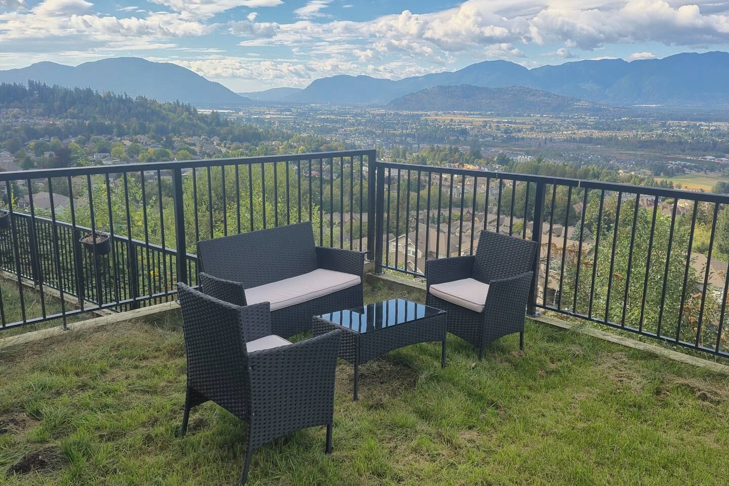 A balcony with wicker furniture and a glass table, overlooking a mountainous landscape.