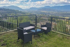 A balcony with wicker furniture and a glass table, overlooking a mountainous landscape.