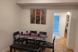 Un coin repas avec une table dressée pour quatre personnes, un banc et un couloir menant à une autre pièce.
