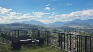 Un balcon aménagé avec du mobilier d’extérieur, offrant une vue sur le paysage urbain et les montagnes.