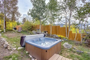 Ein Whirlpool in einem Garten mit Holzterrasse, umgeben von Bäumen und einem Holzzaun.