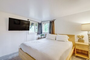 Ein Schlafzimmer mit einem Bett, einem an der Wand befestigten Fernseher, einem Nachttisch und einer Lampe.