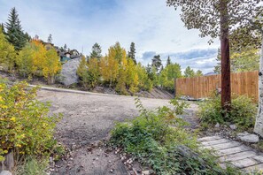 A gravel driveway leading to a wooden fence, surrounded by trees with autumn foliage, and a clear sky. - Mtn-View Cabin Escape in Heart of Grand Lake (Grand Lake)