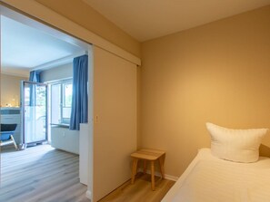 A bedroom with a bed, a small wooden stool, and a sliding door leading to a balcony. - 1 "seestern" in Haus Colonia (St. Peter-Ording)