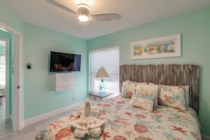 Ein Schlafzimmer mit einem Bett, einem Fernseher, einem Deckenventilator und einem Fenster mit Jalousien.
