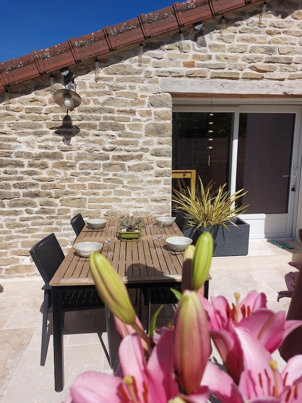 Un espace extérieur aménagé pour les repas, avec un mur en pierre, une table en bois, des chaises et des plantes en pot.