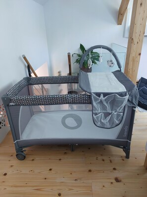 Ein Babybett mit Moskitonetz und gemusterten Kissen, auf einem Holzboden, in der Nähe befinden sich eine Pflanze und Spielzeug.