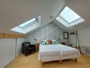 Ein Schlafzimmer mit schrägem Dach, Dachfenstern, einem Bett, einem Sessel und einem Nachttisch.