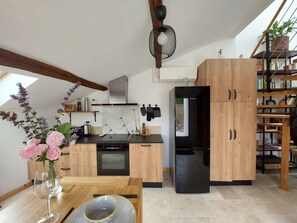 A modern kitchen with wooden cabinets, a black refrigerator, and a dining area with a vase of flowers.