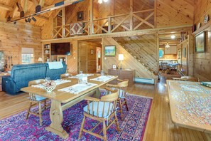 Accogliente interno di una baita in legno, con zona pranzo, soggiorno con divano e una scala che conduce a un piano superiore.