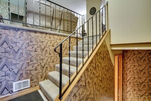 A staircase with geometric patterned walls, a metal handrail, and a carpeted landing.