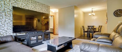 Una sala de estar con televisión de pantalla plana, sofás de cuero, una mesa de centro y un comedor con candelabro.