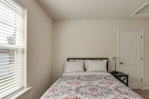 A bedroom with a bed, a nightstand, a door, and a window with blinds. - Dunkirk Group Getaway w/ Easy D.C. Access! (Dunkirk)