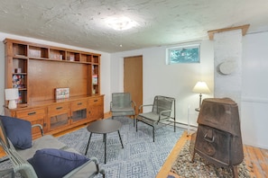 A cozy living room with a wooden entertainment center, two chairs, a small table, a fireplace, and a window. - Deck & Private Trails! Hancock Forest Hideaway (Hancock)