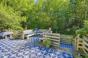 An outdoor seating area with wooden benches and tables, surrounded by lush greenery. - Deck & Private Trails! Hancock Forest Hideaway (Hancock)