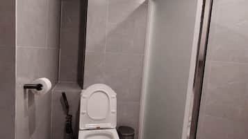 A modern bathroom with a toilet, a hand dryer, and a trash bin.