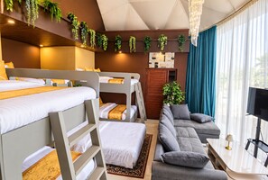 Habitación de hotel con literas, un sofá, un televisor y un ventanal con cortinas.