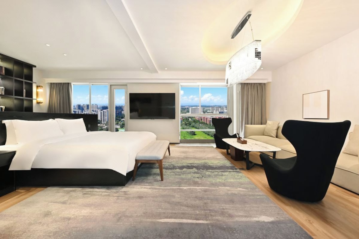 A modern hotel room with a large bed, a sofa, a TV, and a view of the city.