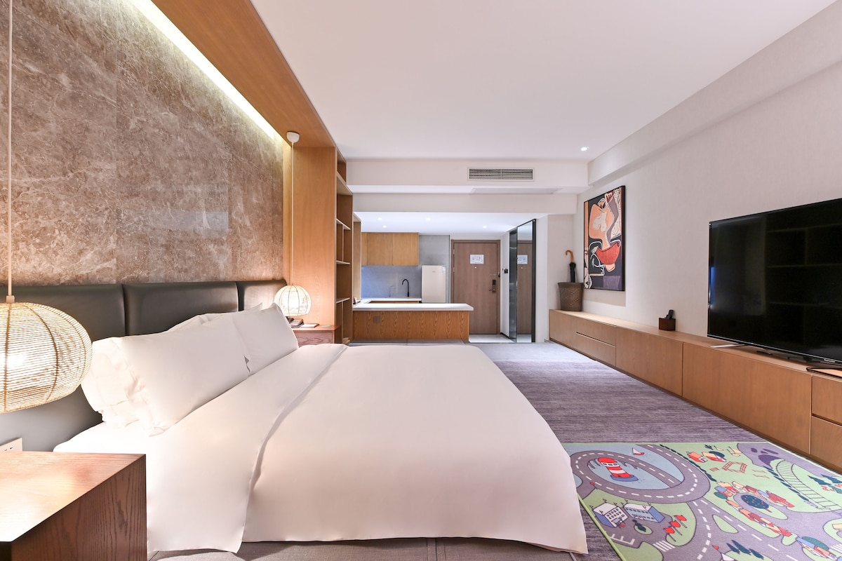 A hotel room with a large bed, a television, a desk, and a bathroom visible in the background.