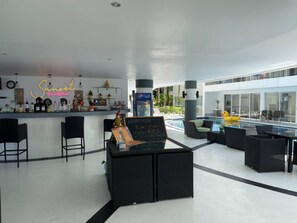 Zona de bar moderna amb un cartell de neó, una zona d'estar a la piscina i un senyal que indica els horaris de l'hora feliç.