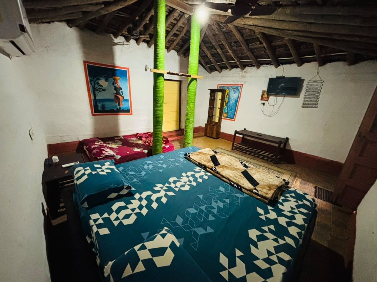 A room with a bed, a bench, a door, and a wall with a painting.