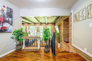 A hallway with wooden flooring, a staircase with a brick wall, and a view of a garden through a window. - Serene Forest Hideaway in Heart of Raleigh (Raleigh)