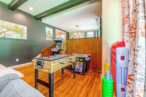 A room with a foosball table, wooden flooring, and a green wall with artwork. - Serene Forest Hideaway in Heart of Raleigh (Raleigh)