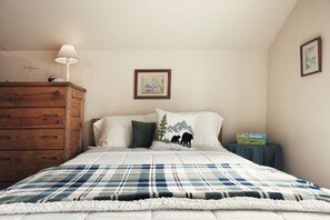Ein Schlafzimmer mit einem Bett, einem Schminktisch, einer Lampe, einem gerahmten Bild und einem kleinen Tisch mit einer Kiste.