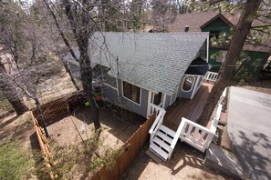 Ein Haus mit geneigtem Dach, einem umzäunten Garten und einer Holzterrasse.