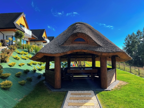 A thatched-roof gazebo with a wooden bench and a pathway leading to it.