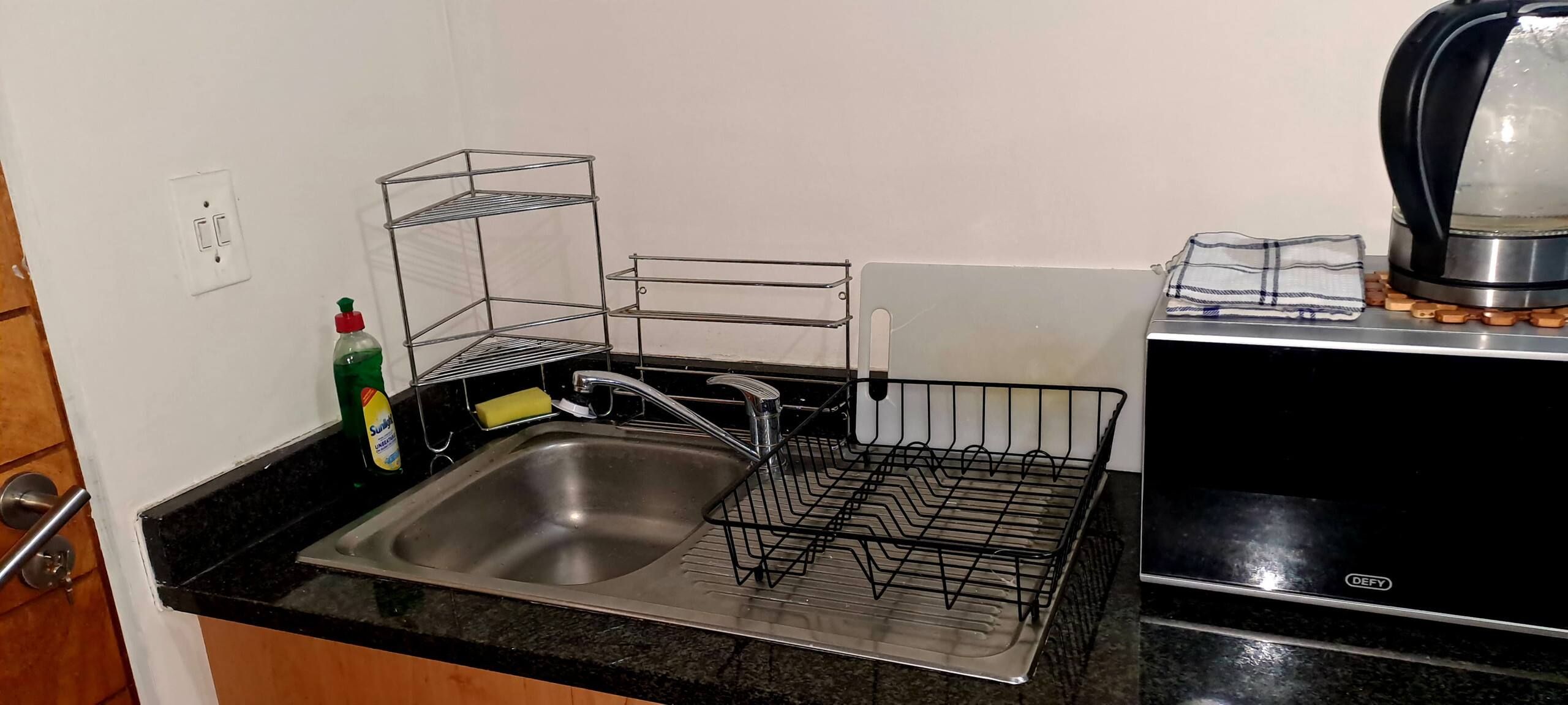 A kitchen with a stainless steel sink, a coffee maker, and a dish rack.