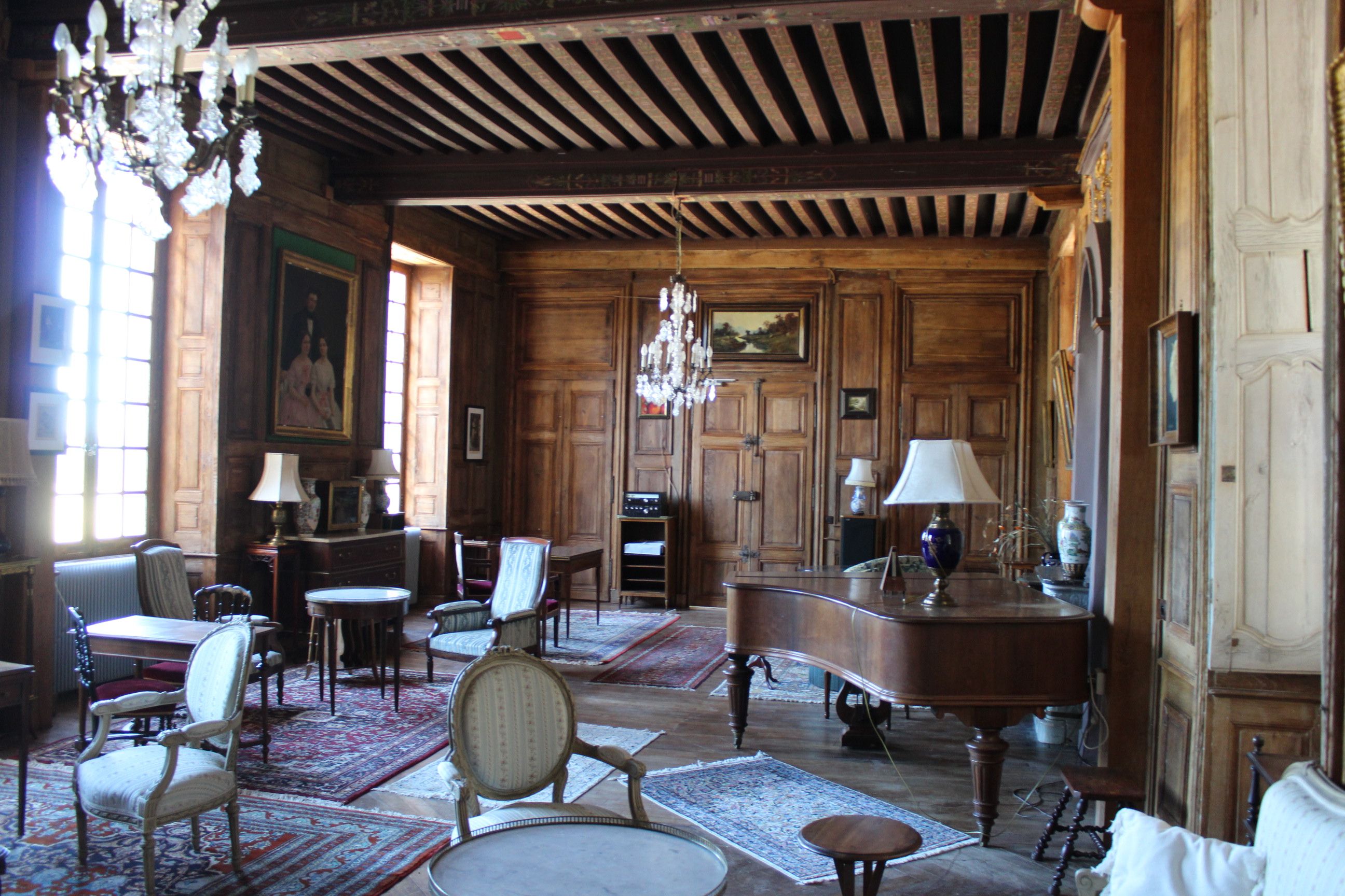 Une pièce spacieuse avec des boiseries, un lustre et divers sièges, notamment un canapé, des fauteuils et une table.